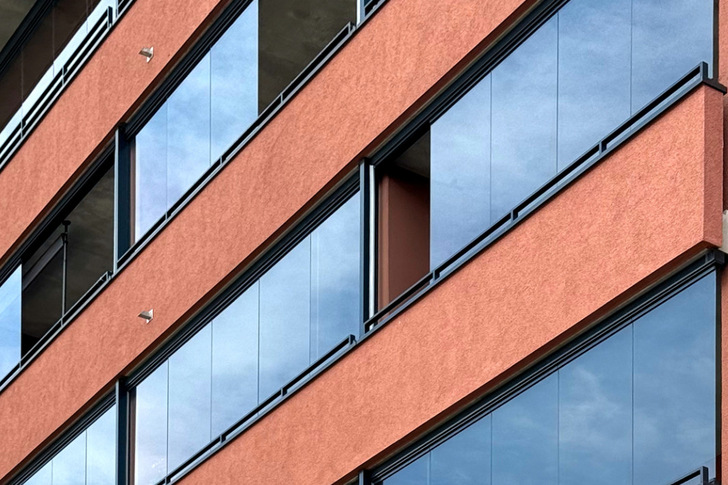 Close-up of a modern building with orange walls and large reflective windows stretching across the façade. - © Lumon