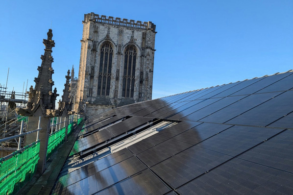 Solar panels on a roof near a historic stone tower under clear blue skies. - © ACT