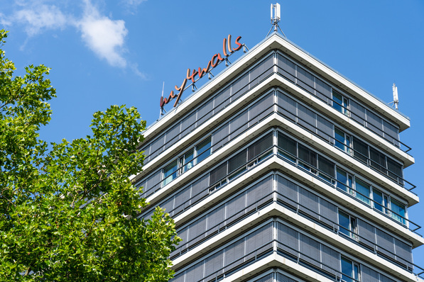 Modern building with "cityflats" sign, surrounded by trees under a clear blue sky. - © Hueck System GmbH