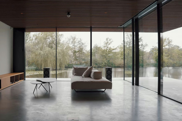 Minimalist living room with a sofa, table, and large windows overlooking a serene lake surrounded by trees. - © Keller minimal windows