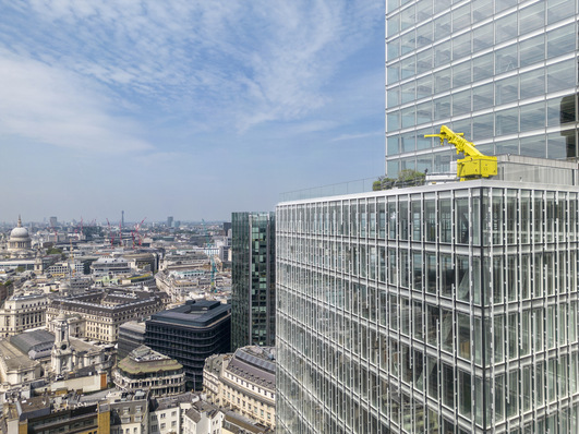 Cityscape view with modern glass buildings, featuring a distinctive yellow crane on a rooftop, under a blue sky. - © Dirk Lindner
