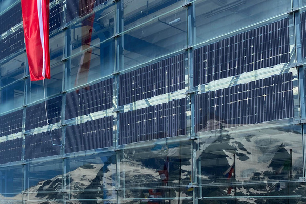 Solar panels on a building with mountain reflections. A red flag is visible to the left. - © Malte Forstat / GW-News