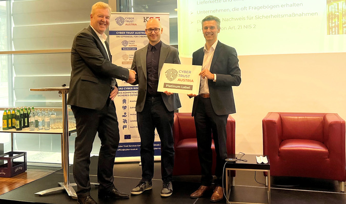 Three men in office attire shaking hands and holding a "Cyber Trust Austria - Platinum Label" certificate. - © Lisec