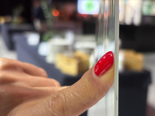 Eine Hand mit rotem Nagellack hält eine dünne Glasplatte, ein unscharfer Hintergrund ist sichtbar. - © Matthias Rehberger / GW