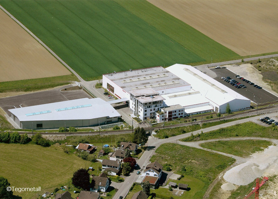 Luftaufnahme eines großen industriellen Gebäudekomplexes in der Nähe von Feldern und Wohnhäusern. - © Swisspacer