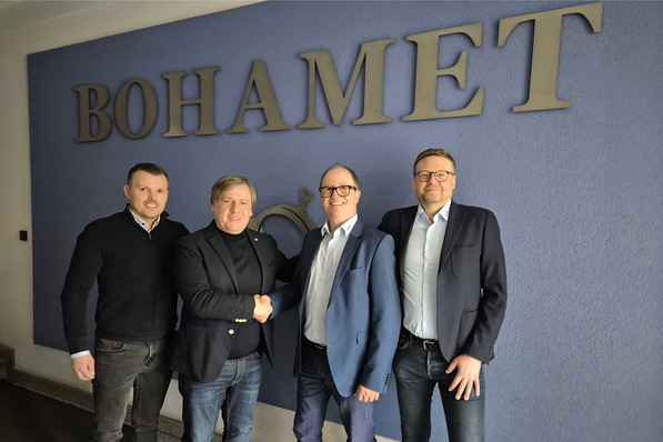Vier Männer in Geschäftskleidung stehen lächelnd vor einer blauen Wand, auf der das Wort "BOHAMET" steht. - © A+W Software / Bahomet S.A.