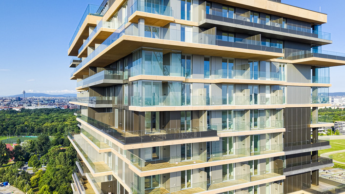 Modernes gläsernes Wohnhaus mit großzügigen Balkonen, die an klaren Tagen einen Blick auf die Stadt und eine grüne Parkanlage bieten. - © Glas Marte/Bildszene Werbe GmbH