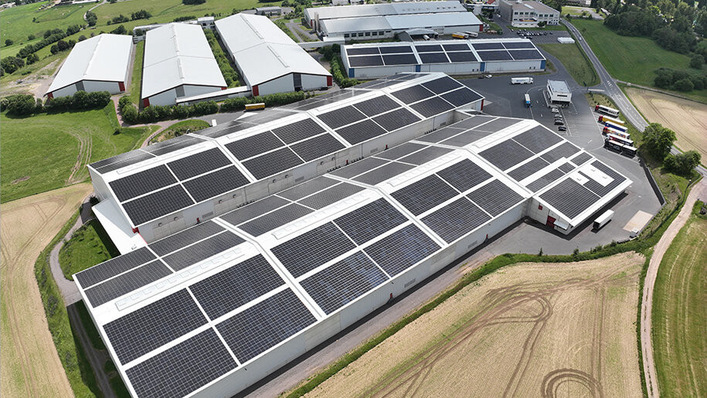 Luftaufnahme von großen Industriegebäuden mit Solarzellen auf den Dächern, umgeben von Feldern und Straßen. - © Wiegand-Glas